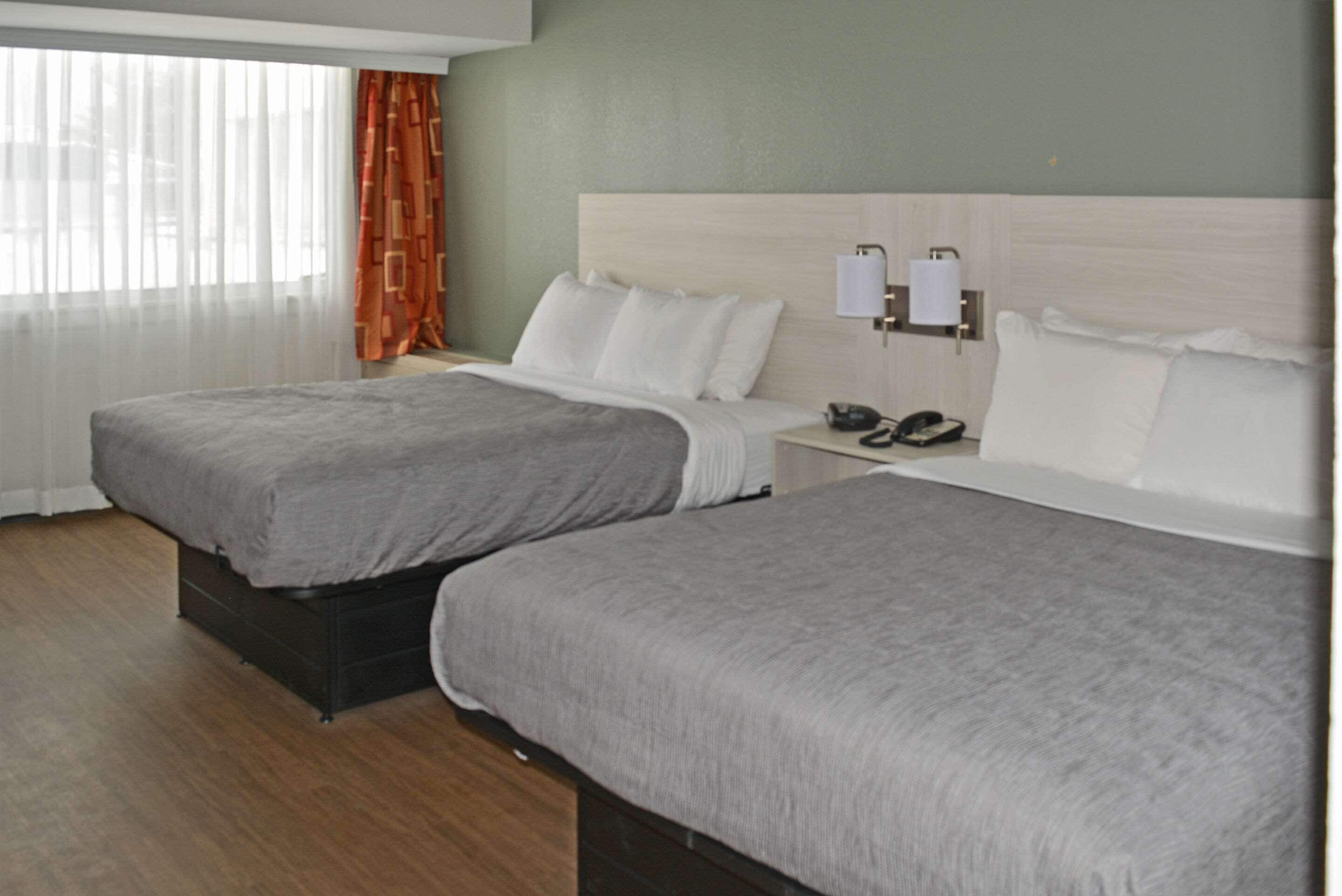 A hotel room with two beds, a nightstand with a phone, and a window with curtains.