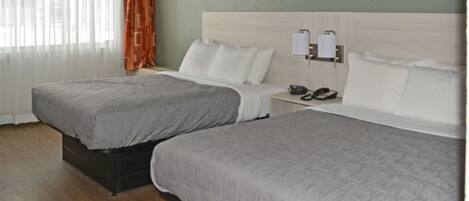 A hotel room with two beds, a nightstand with a phone, and a window with curtains.