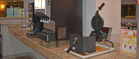 A self-service coffee station with a waffle maker and a coffee machine.