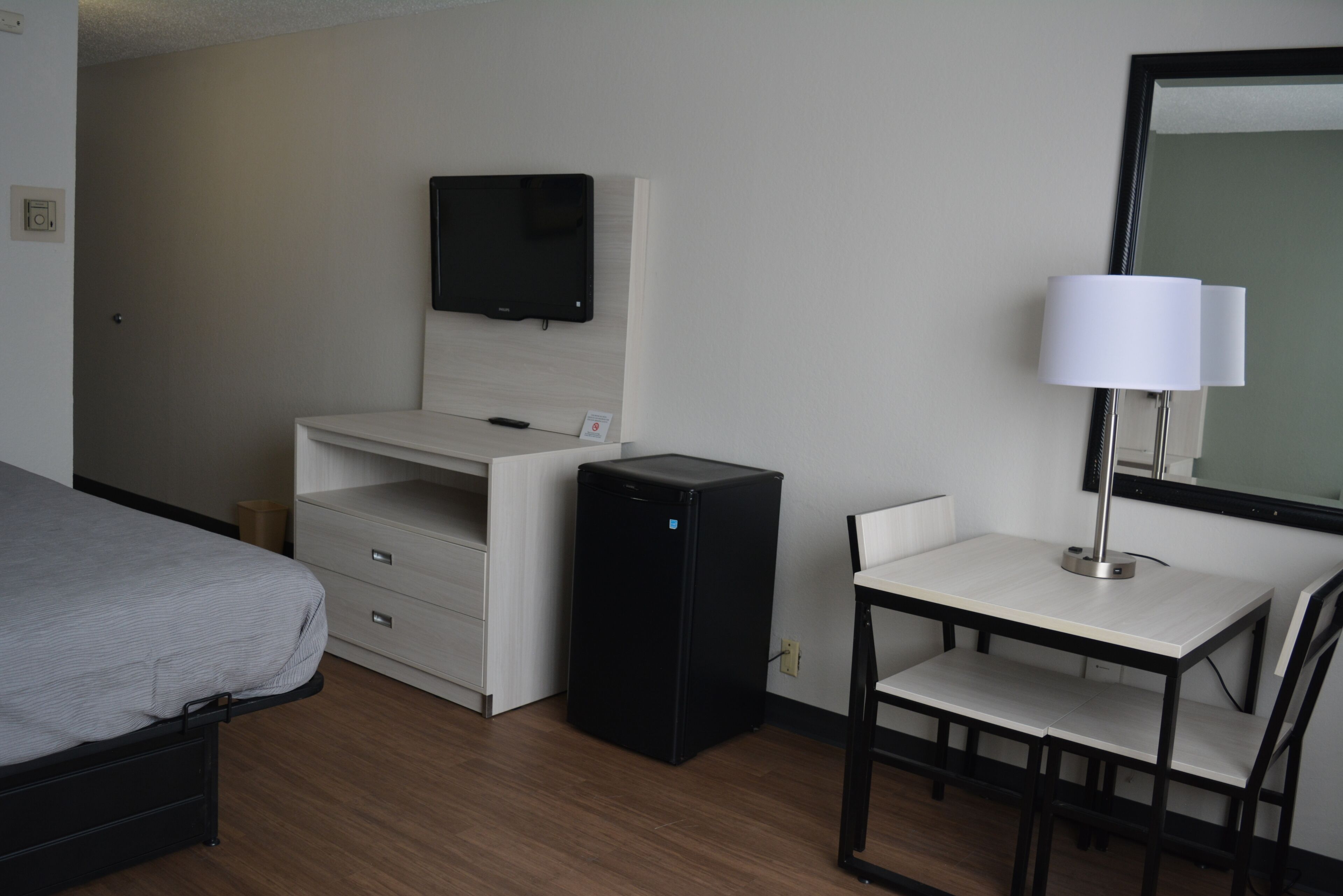 A hotel room with a bed, a desk with a computer, a TV, and a lamp.