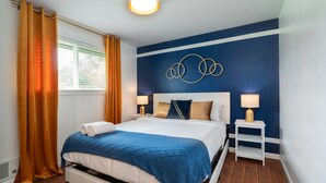 A hotel room with a bed, two bedside tables, a wall art piece, and a window with curtains.