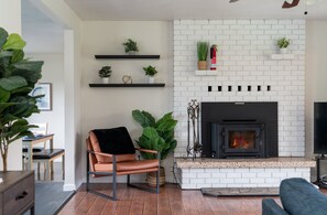 Un salon avec une cheminée, un canapé, un fauteuil et des plantes en pot.