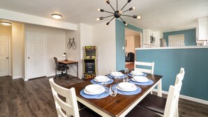 A dining area with a wooden table set for six, white chairs, and a ceiling light fixture.
