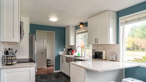 A modern kitchen with white cabinets, a granite countertop, and a window with a view of trees.