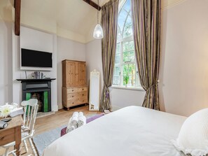 A bedroom with a bed, a wooden wardrobe, a television, and a window with curtains.