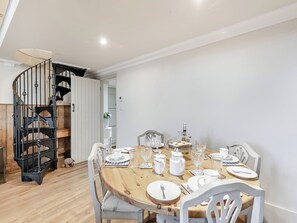 A dining area with a wooden table set for four, white chairs, and a black spiral staircase in the background.