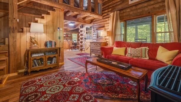 L’intérieur d’une cabane en rondins, avec un canapé rouge, des meubles en bois et un tapis à motifs.