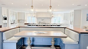 A modern kitchen with a central island featuring a built-in bench, pendant lighting, and a large window providing natural light. - Spacious Home Near Wallis Sands Beach in Rye NH (Rye)