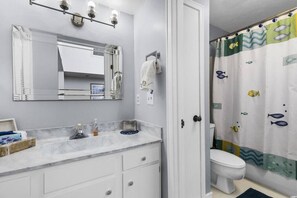 A bathroom with a white vanity, a mirror, a towel rack, and a shower curtain with fish designs.