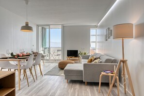 Ett modernt vardagsrum med en grå soffa, ett matbord med stolar, en tv och en lampa.