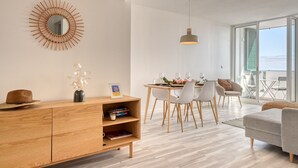 A modern living room with a wooden cabinet, dining table, and chairs. There is a large mirror on the wall and a pendant light above the table.