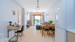 Une cuisine moderne équipée d’un réfrigérateur, d’une table à manger avec des chaises, d’un bureau en bois avec une chaise et d’un téléviseur.