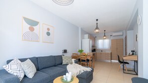 Un salon moderne avec un canapé gris, un coin repas avec une table et des chaises en bois, et une cuisine en arrière-plan.