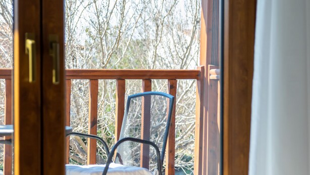 Une pièce avec un lit, une chaise et une vue sur les arbres, visible par une porte ouverte.