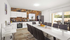 A modern kitchen with white cabinets, a stone backsplash, and a dining area with a white table and chairs. - Villa Nur Amela - Pool, Jacuzzi, Darts (Pula)
