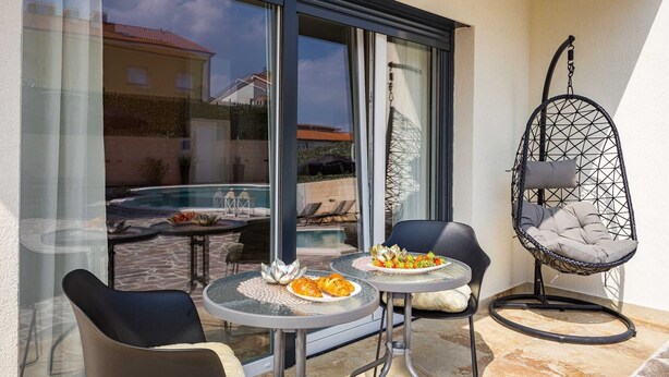 A balcony with two round tables, chairs, and a hanging chair. - Villa Nur Amela - Pool, Jacuzzi, Darts (Pula)