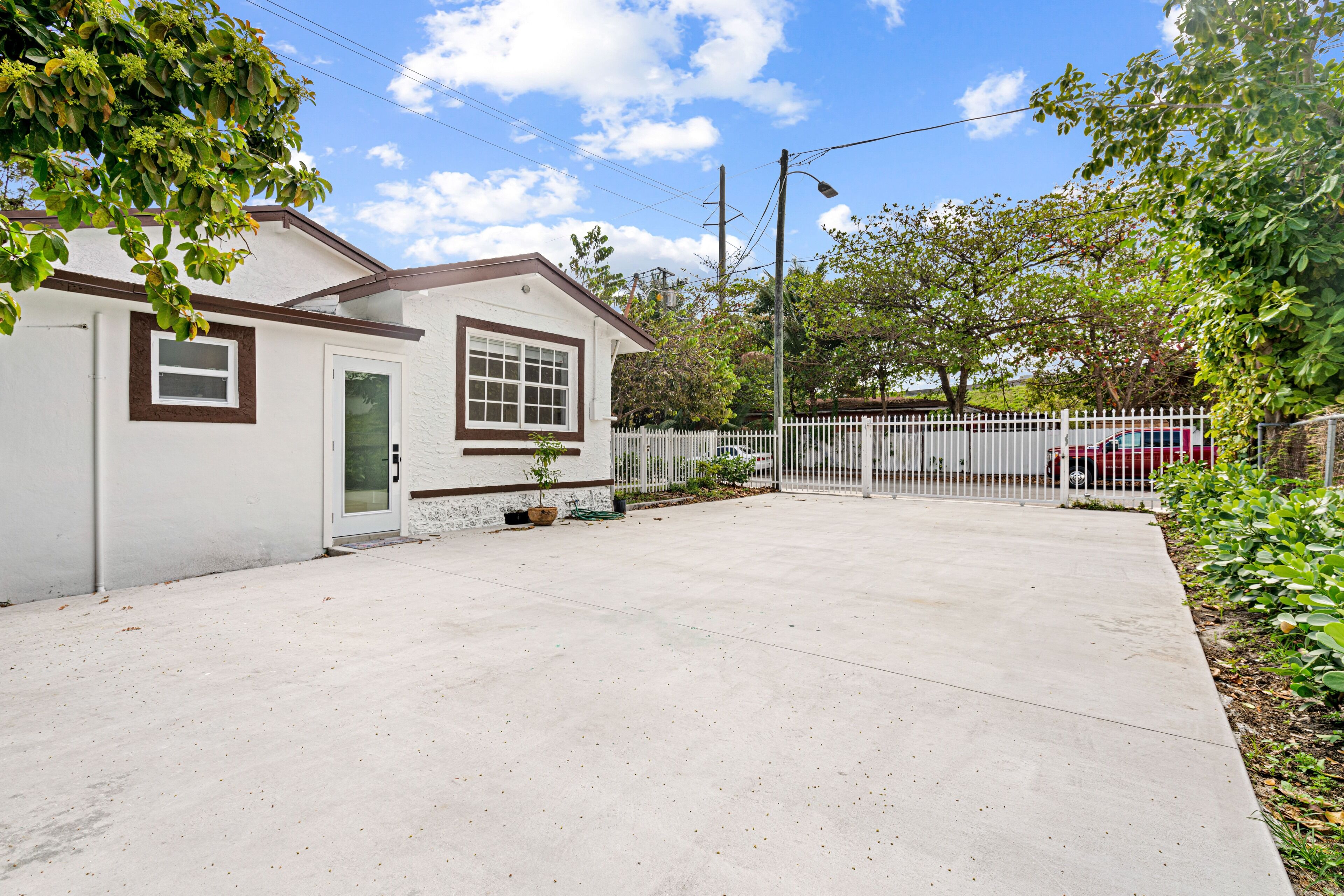 A single-story house with a white exterior and brown trim, a front door, and a small front yard with a white picket fence.