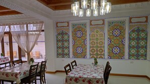 A dining area with tables set for four, wooden chairs, and a chandelier. - Nostalgia boutique hotel (Bukhara)