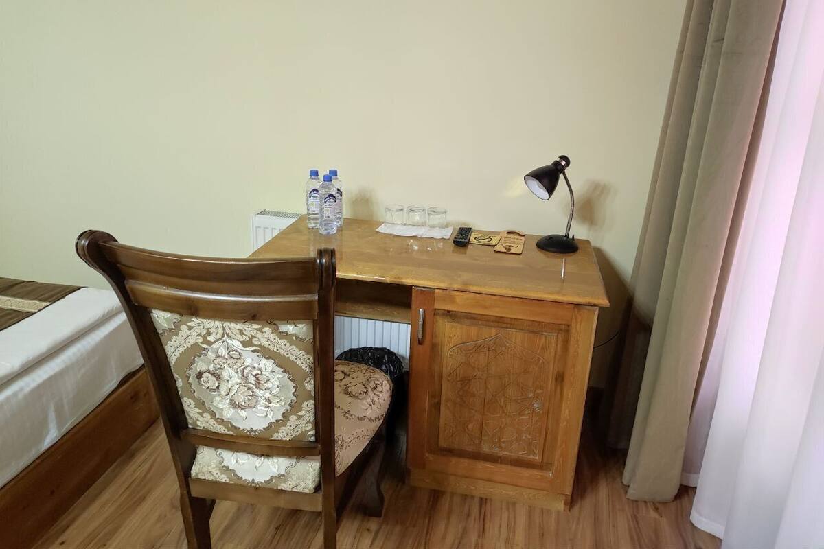 A wooden desk with a chair, a lamp, and a small cabinet. There are bottles and glasses on the desk.