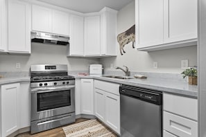 A modern kitchen with white cabinetry, stainless steel appliances, and a marble countertop. - Sunrise Condo in Convenient Provo Location (Provo)