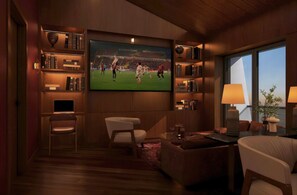 A modern living room with a flat-screen TV mounted on the wall, a bookshelf, a comfortable seating area with a sofa and armchairs, and a large window providing a view of the outdoors. - Holiday Inn Hotel And Suites Kocaeli Dilovasi Gulf View by IHG (Dilovasi)