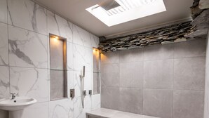 Een moderne badkamer met een marmeren wastafel, een glazen douchecabine en een accentmuur van steen.