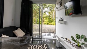 Een moderne woonkamer met een zwarte bank, een glazen salontafel en een flatscreen televisie aan de muur.