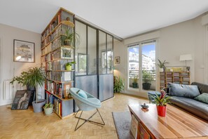 A modern living room with a bookshelf, a blue chair, a sofa, and a wooden coffee table. - 90 m2 chic, cosy, bright, modern, 6 mn from Paris on foot, 3 mn from the metro (Les Lilas)
