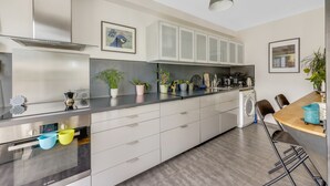 Une cuisine moderne équipée d’un four encastré, d’un lave-linge et d’un coin repas avec des tabourets de bar.