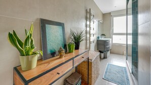 Une salle de bain moderne avec un meuble-lavabo en bois, des plantes en pot, une œuvre d’art encadrée et une cabine de douche en verre.
