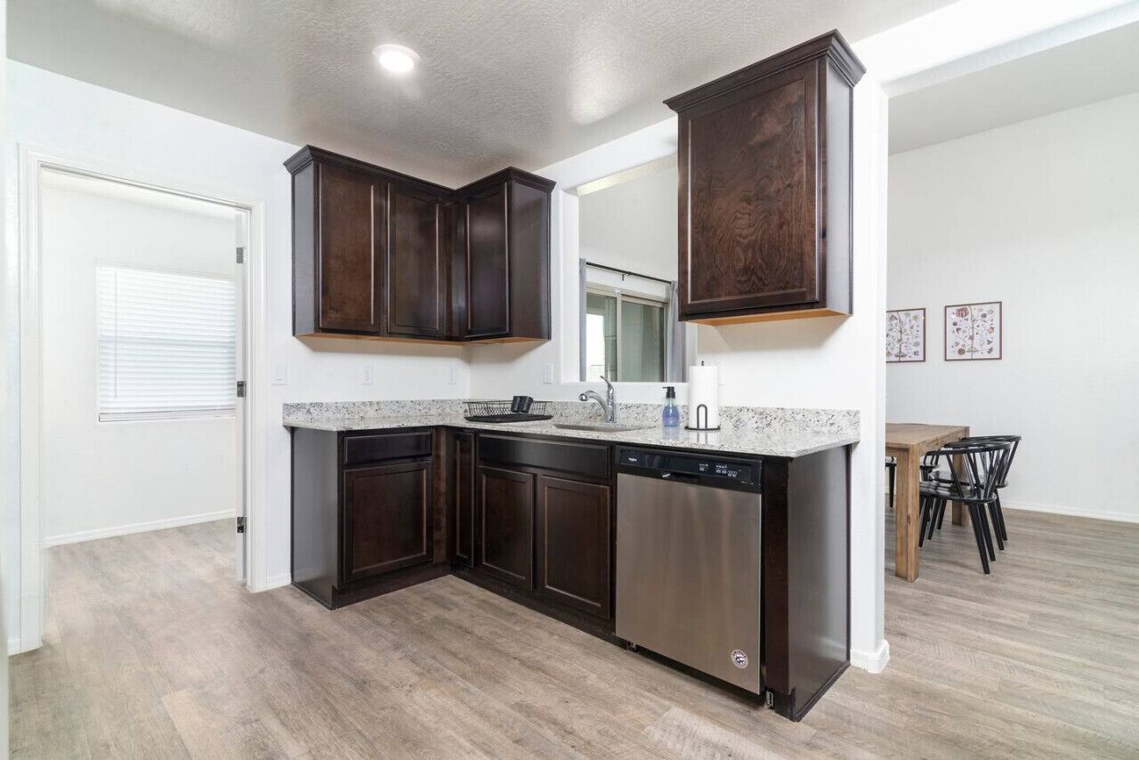 A modern kitchen with dark wood cabinets, a stainless steel dishwasher, and a granite countertop.