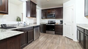 A modern kitchen with dark wood cabinets, stainless steel appliances, and a granite countertop. - *Spacious Family Oasis*Pool Table*Backyard*Garage* (Casa Grande)