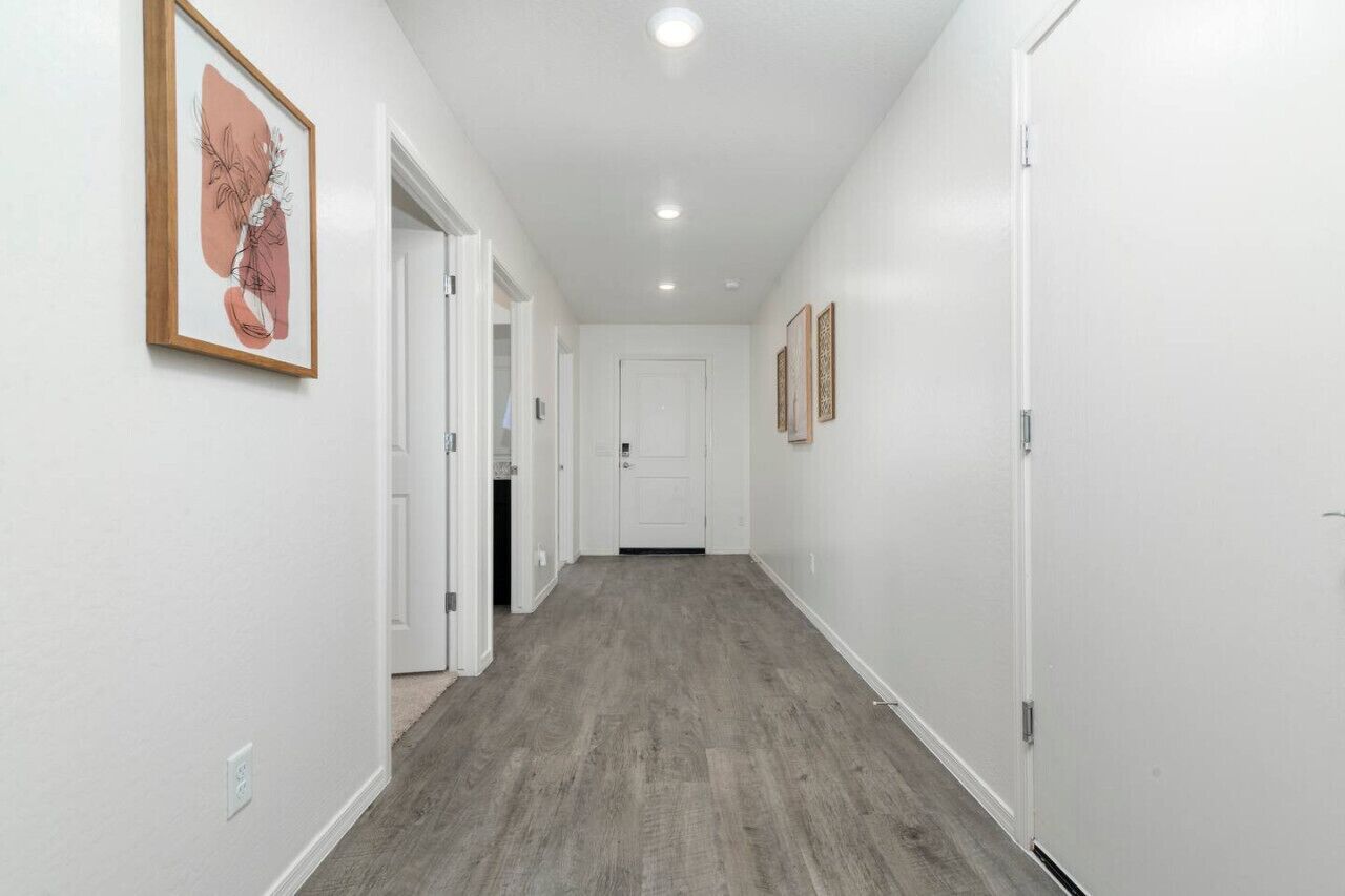 A hallway with white walls and a grey floor, leading to a white door at the end.