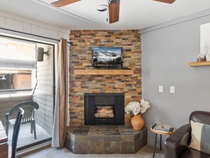 A living room with a stone fireplace, a mounted TV, and a wooden shelf.