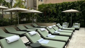 Fila de sillones verdes con toallas y tumbonas, dispuestas en un patio empedrado con sombrillas que ofrecen sombra.