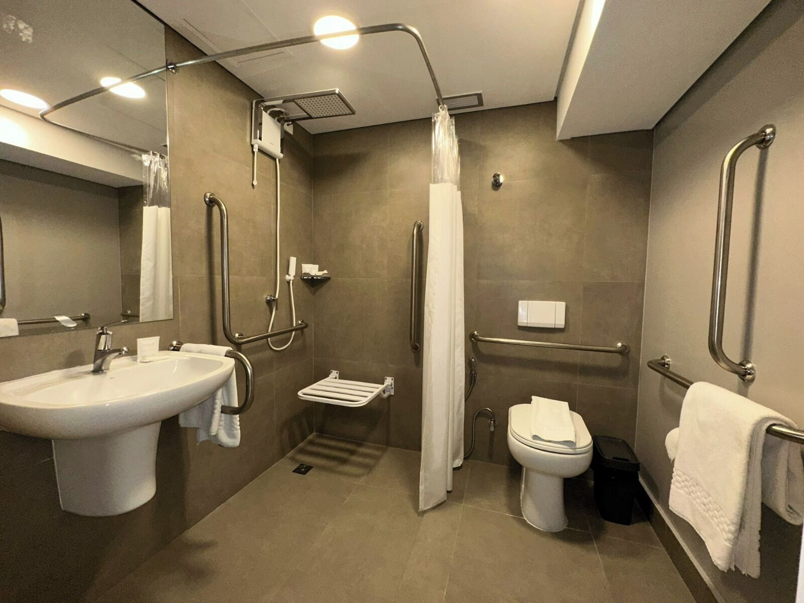 A modern bathroom with a sink, toilet, shower, and grab bars.