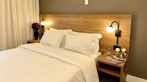 Una cama bien hecha con sábanas blancas, un cabecero de madera y dos lámparas de noche.