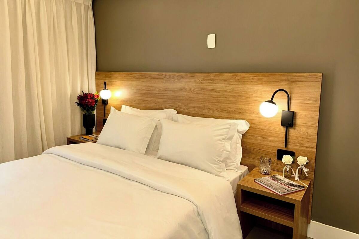 Una cama bien hecha con sábanas blancas, un cabecero de madera y dos lámparas de noche.