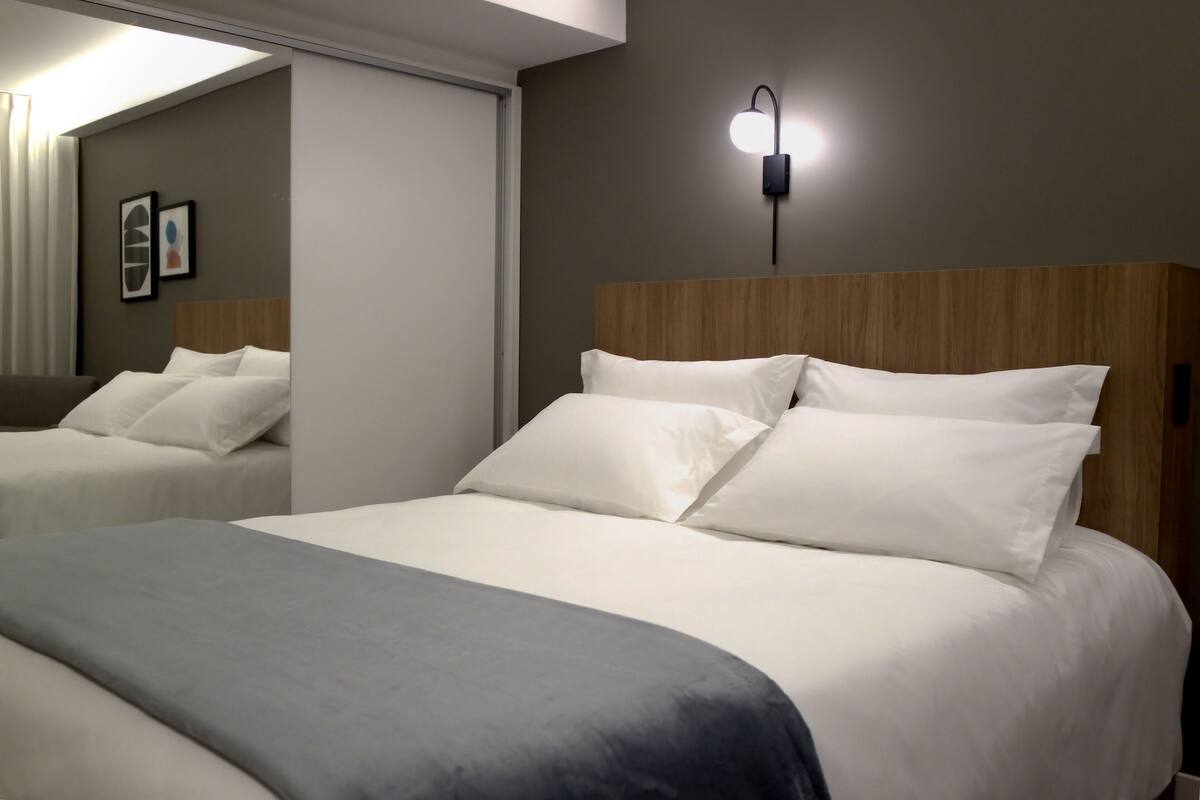 Una habitación de hotel con una cama grande, una mesita de noche, una lámpara de pared y un espejo.