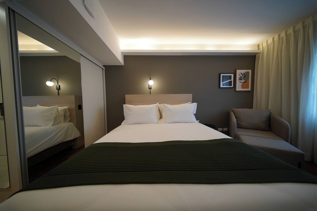 Habitación de hotel con una cama grande, dos lámparas de noche, un sofá y una obra de arte colgada en la pared.