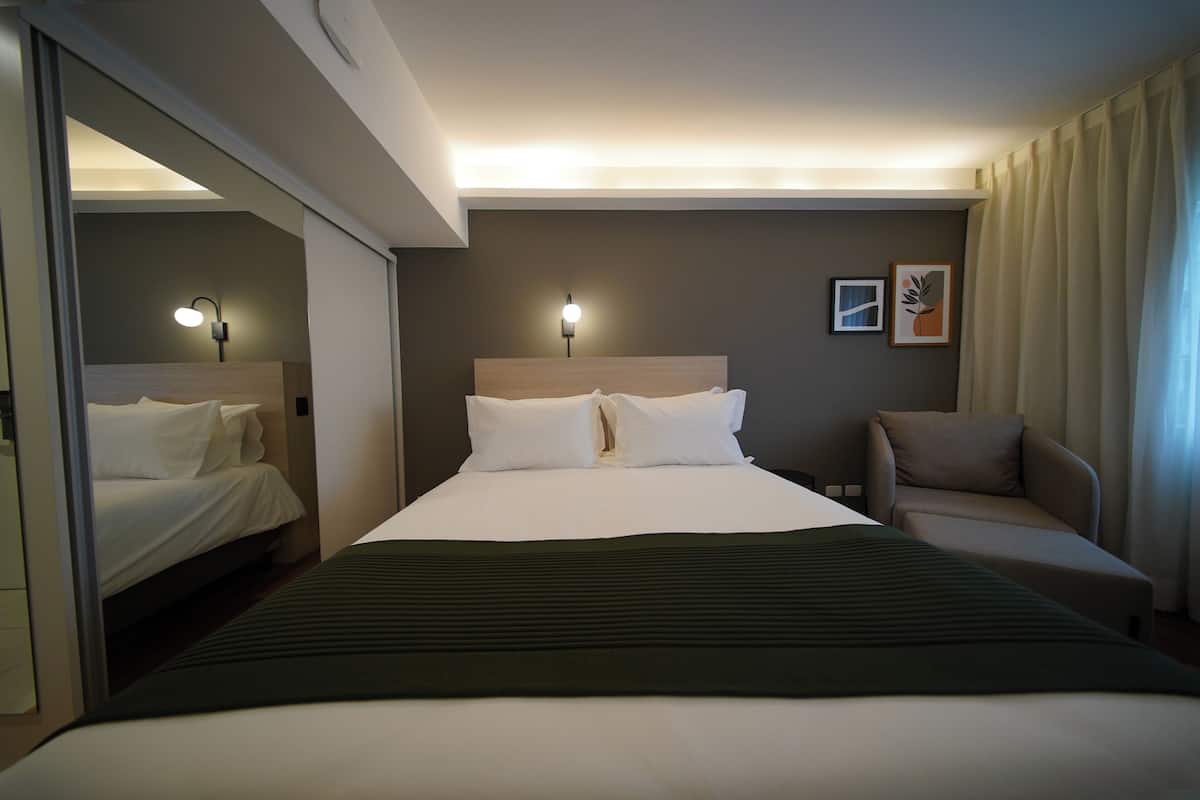 Une chambre d’hôtel avec un grand lit, deux lampes de chevet, un canapé et une œuvre d’art accrochée au mur.