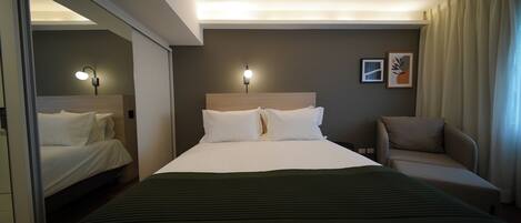 A hotel room with a large bed, two bedside lamps, a sofa, and a wall-mounted artwork.