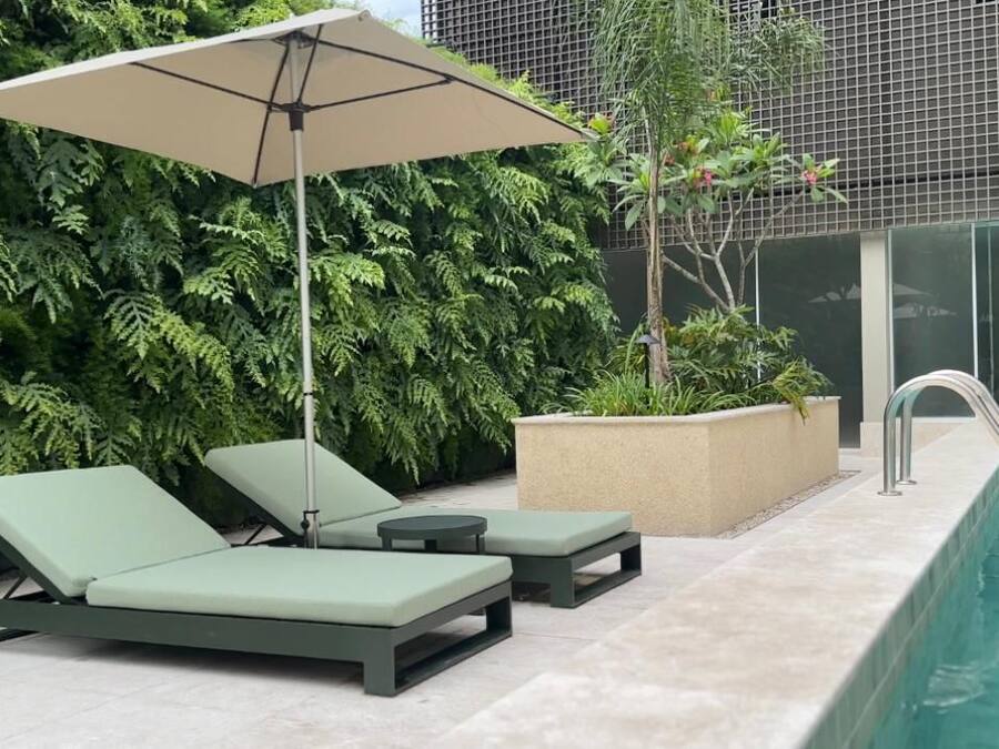 A poolside area with lounge chairs and a canopy, surrounded by lush greenery and a modern building in the background.
