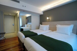 Hotellihuone, jossa on kaksi sänkyä, peili, yöpöytä ja seinään kiinnitetty valaisin.
