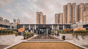 A modern building with a central entrance, surrounded by a courtyard with potted plants and umbrellas. - He Hotel (Liuyang)