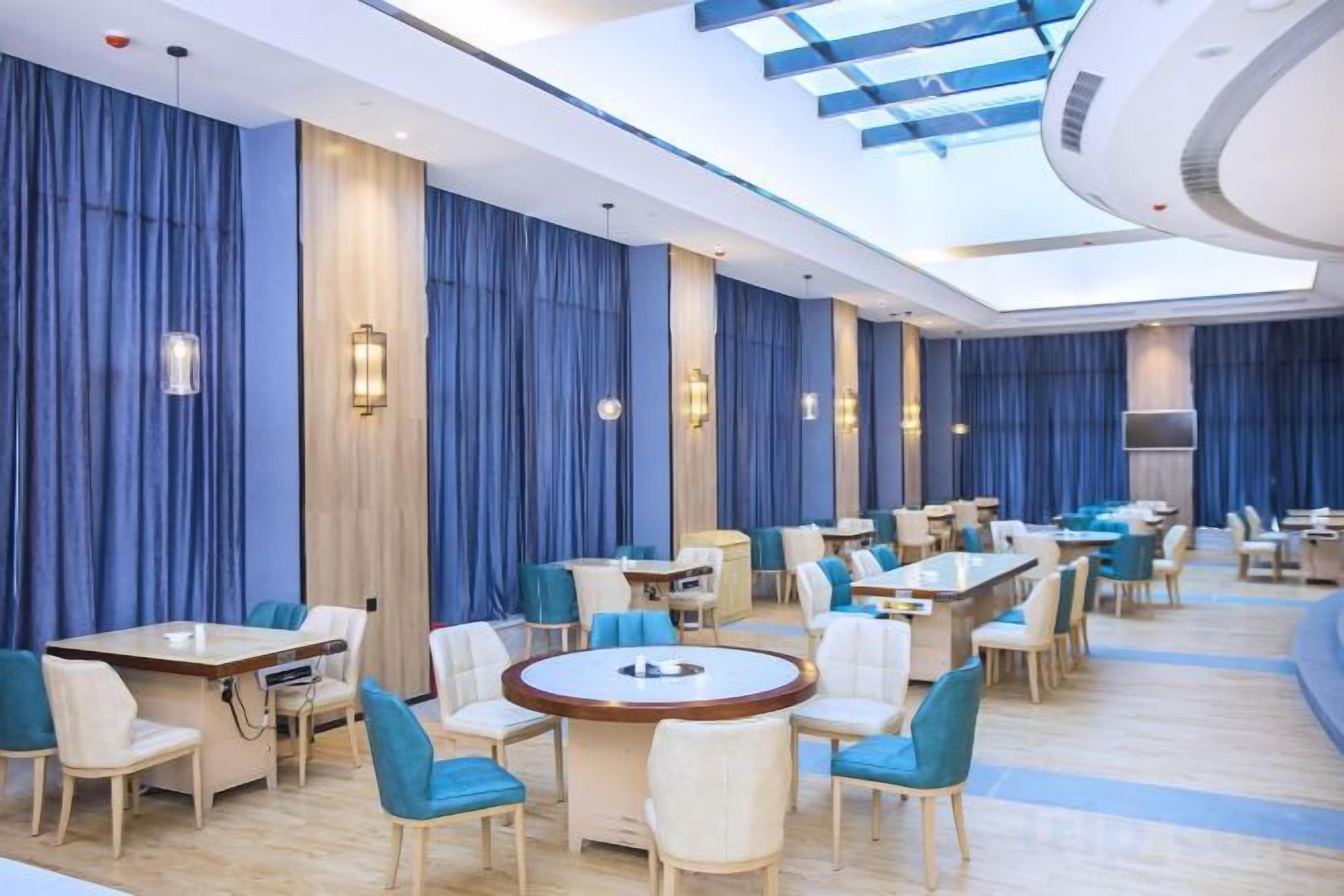 A hotel dining area with round tables, chairs, and blue curtains.