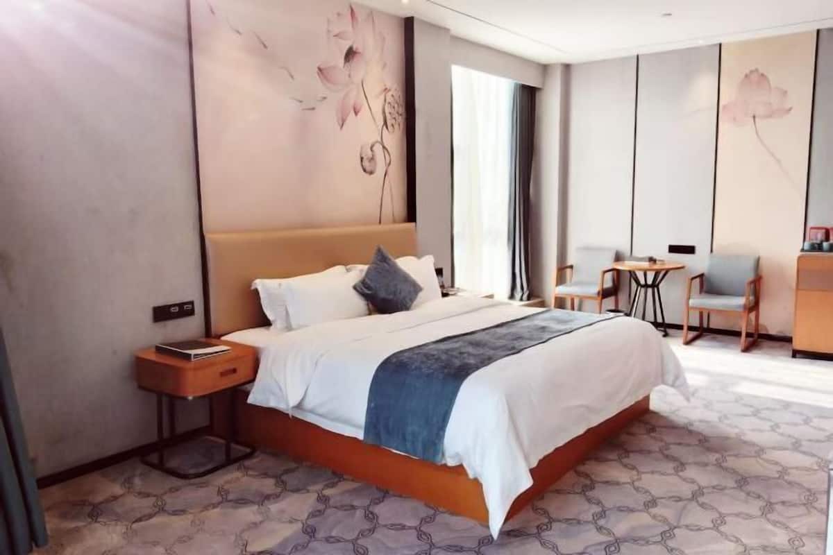 A hotel room with a large bed, a bedside table, a small desk, and a chair.