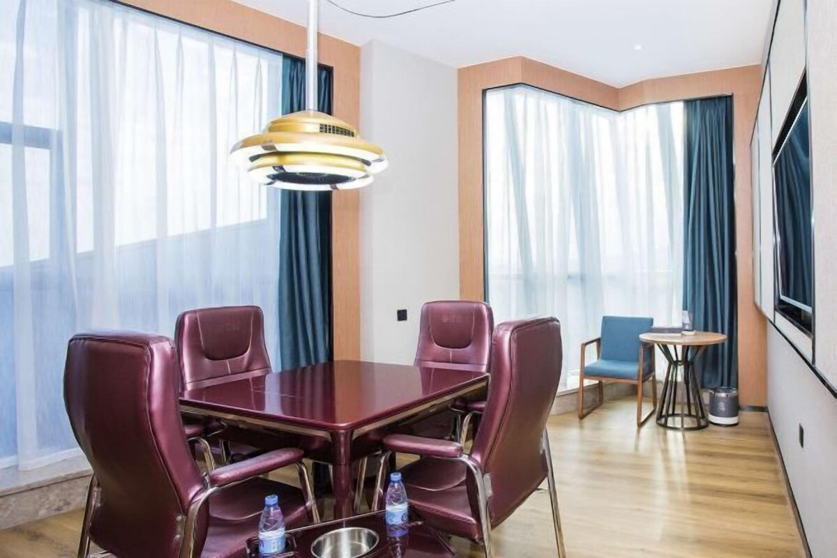 A hotel room with a large dining table, four chairs, a small round table, and a TV mounted on the wall.