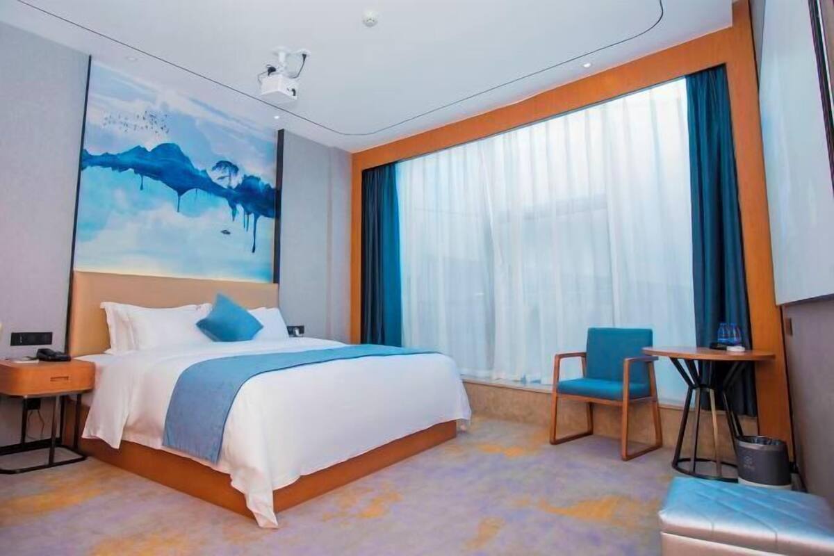 A modern hotel room with a large bed, a desk, a chair, and a painting on the wall.