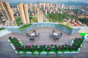 A rooftop terrace with a curved wooden deck, seating area, and flower beds. - He Hotel (Liuyang)